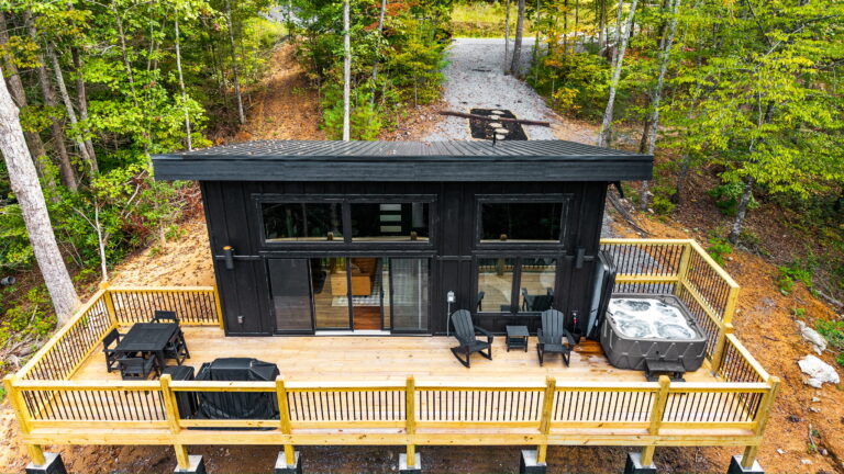 Aerial view of a modern MCHB mini cabin in Gatlinburg, TN, showcasing the full wooden deck, hot tub, BBQ area, and integration into the mountain landscape.
