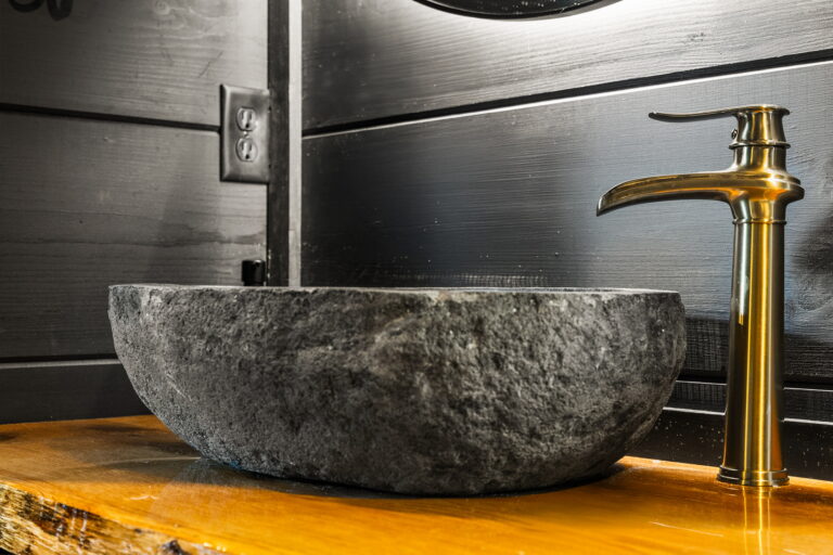 Detail shot of a Spa-Inspired Bathroom sink: elegant carved stone basin and high-end faucet fixture. Luxury Mountain Cabin detail, East TN.
