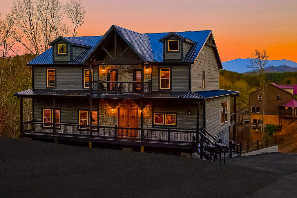 Impressive Luxury Cabin Mansion exterior at sunset. Multi-room home interior lit up, showcasing a warm glow in the Smoky Mountains, TN.