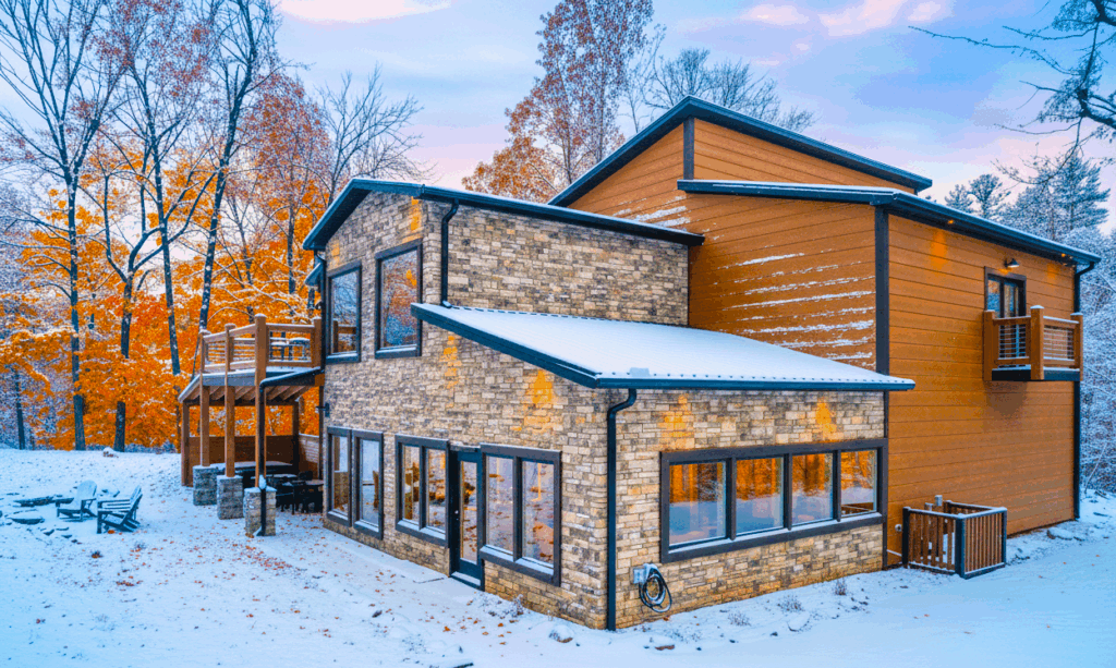 Modern Contemporary Mountain Cabin exterior in the Smoky Mountains. Early snowfall covers the luxury home while autumn trees still show lush colors, East Tennessee.