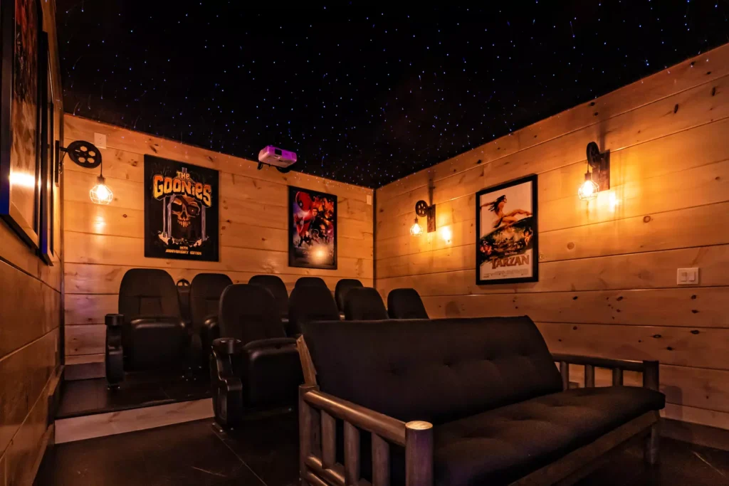 Luxury Cabin In-House Movie Theater with tiered cinema seating, plush headrest chairs, large screen, and movie poster decor. Showcases integration of design and technology in a Smoky Mountain home.