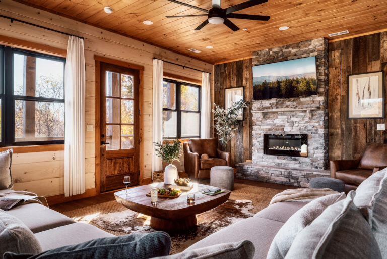 Luxury Mountain Home Living Room at Summit Skies. Features a custom stone fireplace, high-end designer furniture, and exquisite interior decor in a custom-built Smoky Mountain cabin. Captures the specific focal point (fireplace) and emphasizes the "custom-built" nature which is