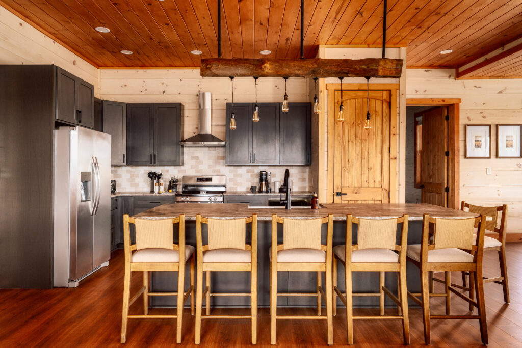 Luxury Mountain Home Kitchen interior at Summit Skies. Features a breakfast bar with high stool chairs, custom lighting, marble quartz countertops, and high-end appliances in a Smoky Mountain custom cabin.