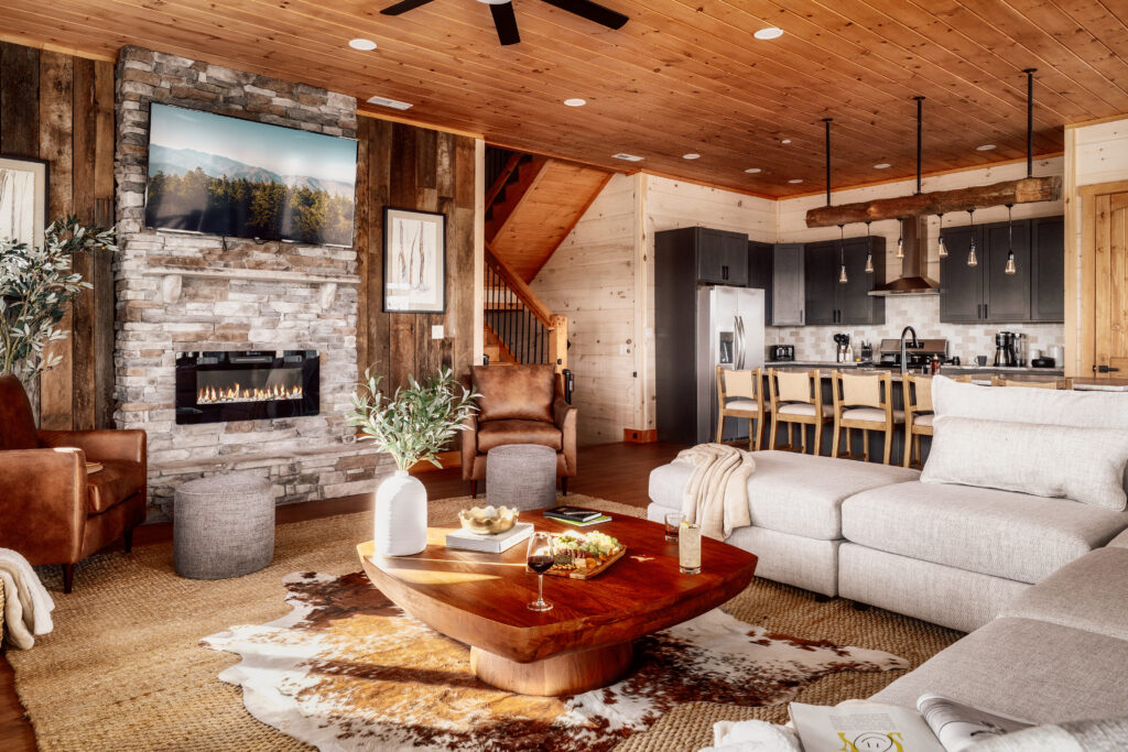 Open-concept living room and kitchen perspective in the Summit Skies luxury mountain home. Showcasing an integrated floor plan with high-end appliances, designer furniture, and custom wood interiors in the Smoky Mountains.