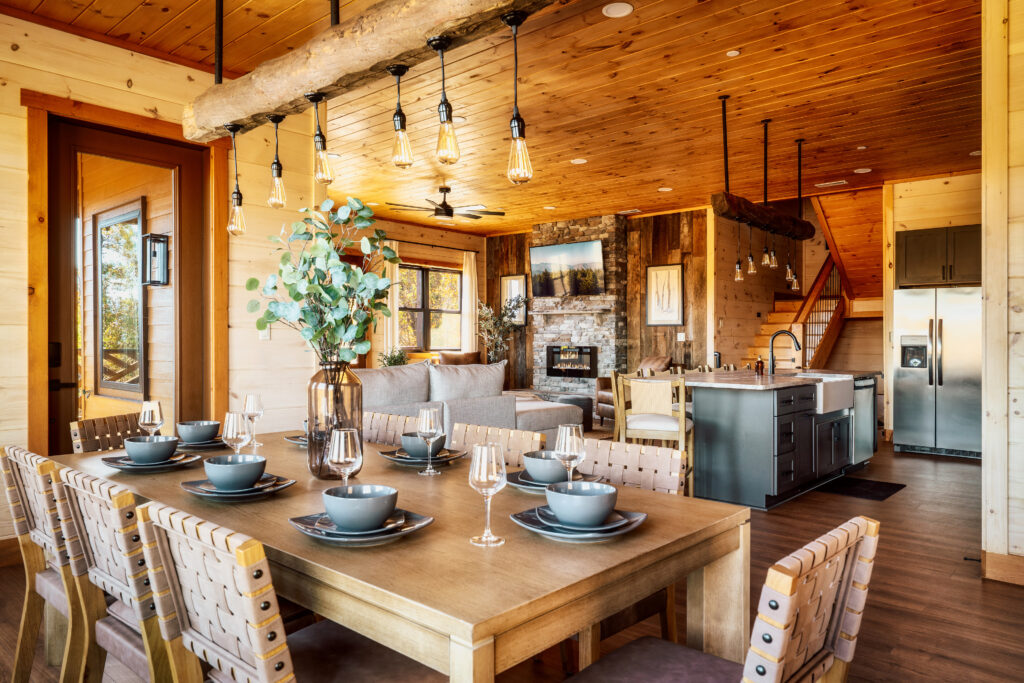 Perspective view from the dining room into the luxury living area of Summit Skies. Features fine interior design, high-end furniture, and a custom stone fireplace in a modern Smoky Mountain cabin.