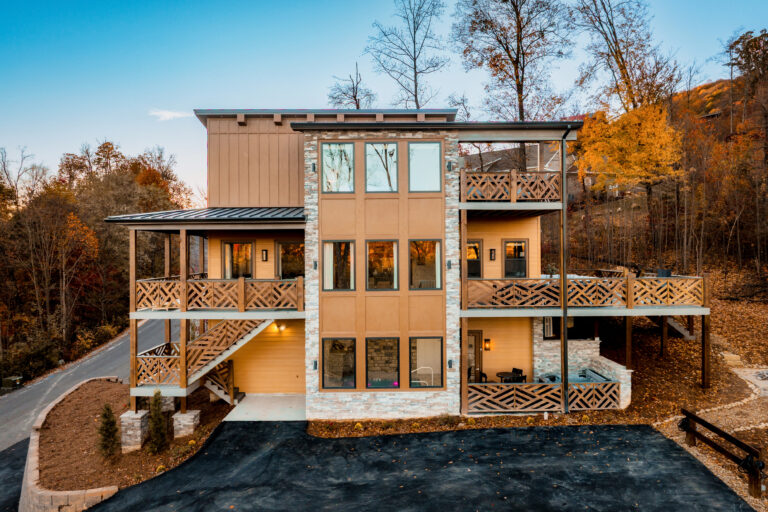 Afternoon exterior shot of Summit Skies, a three-story luxury mountain home by MCHB. Nestled in the Smoky Mountains near Sevierville, TN, surrounded by vibrant autumn foliage and lush mountain landscape.