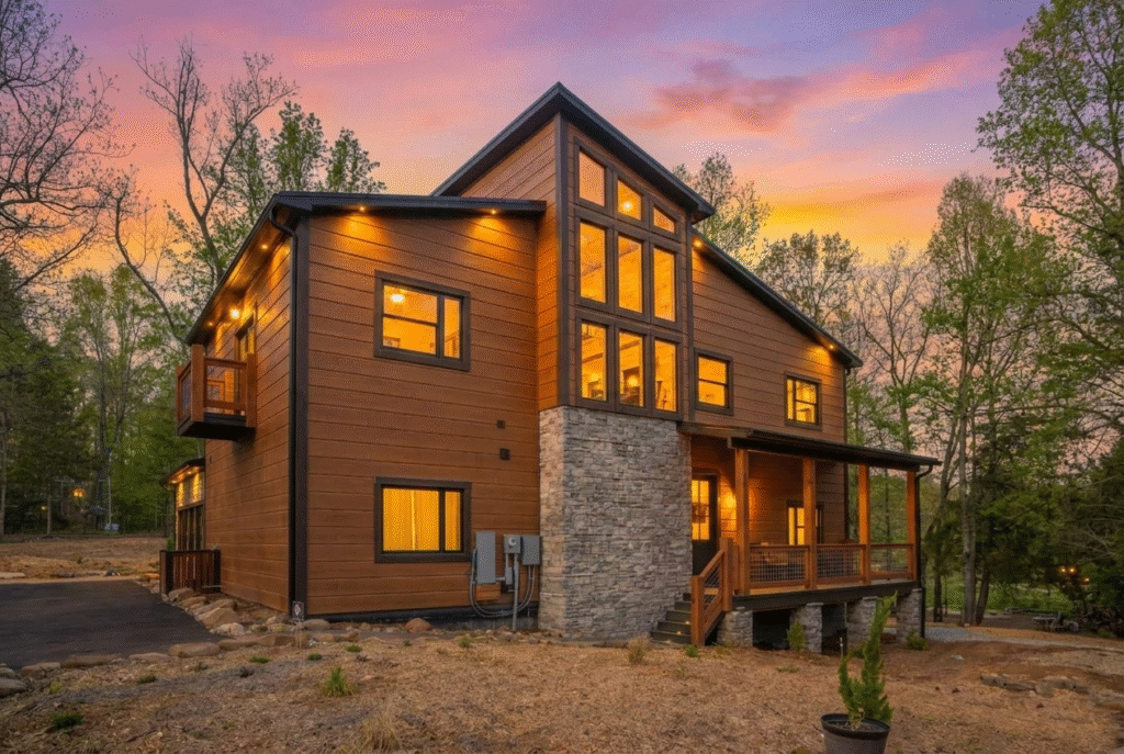 Rear view of a 3-story luxury contemporary mountain home by MCHB at dusk. Features vaulted ceilings, floor-to-ceiling glass, and warm interior lighting in the Smoky Mountains.