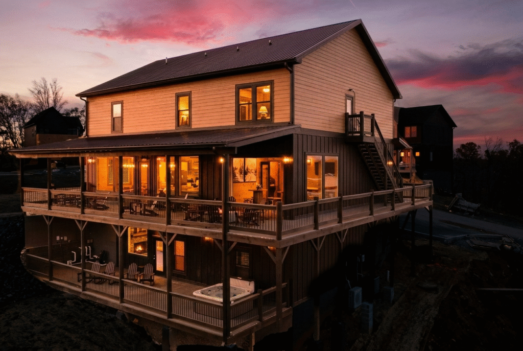 Side view of a 3-story MCHB luxury mountain cabin at dusk. Features spacious terrace balconies, an outdoor hot tub, and cozy, inviting warm lighting.