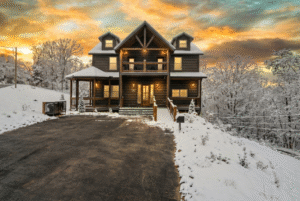 Winter-ready luxury mountain home exterior at sunset, covered in snow. A custom MCHB build in Sevierville, TN, featuring snow-load engineered roofing and premium insulation for the Smoky Mountain climate.