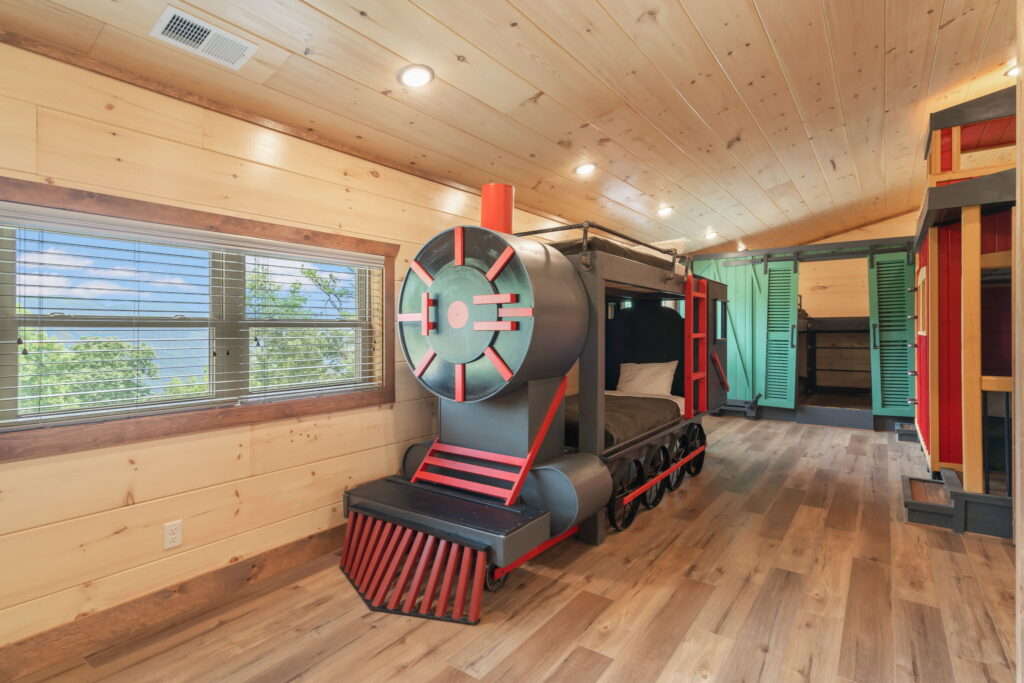 Bespoke children's bunk room inside Shell Mountain Sunrise cabin. Features a built-in "Train Wagon" theme with a custom locomotive machine and play wagons, engineered by MCHB to maximize high-yield family bookings in the Smoky Mountains.
