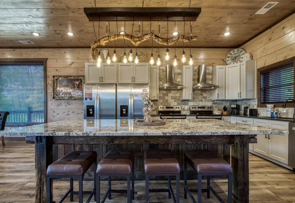 Luxury contemporary traditional kitchen by MCHB in the Smoky Mountains. Features custom lighting, a high-end wood dining table, and integrated modern appliances.
