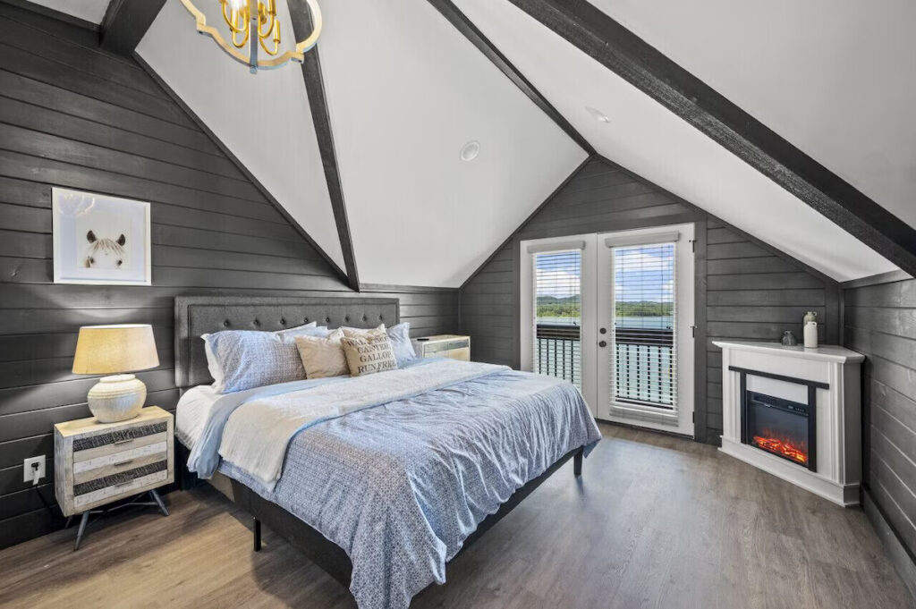 High-end luxury contemporary master suite by MCHB in Gatlinburg, TN. Features a built-in stone fireplace, private balcony access, and designer linens in a fully furnished cabin.