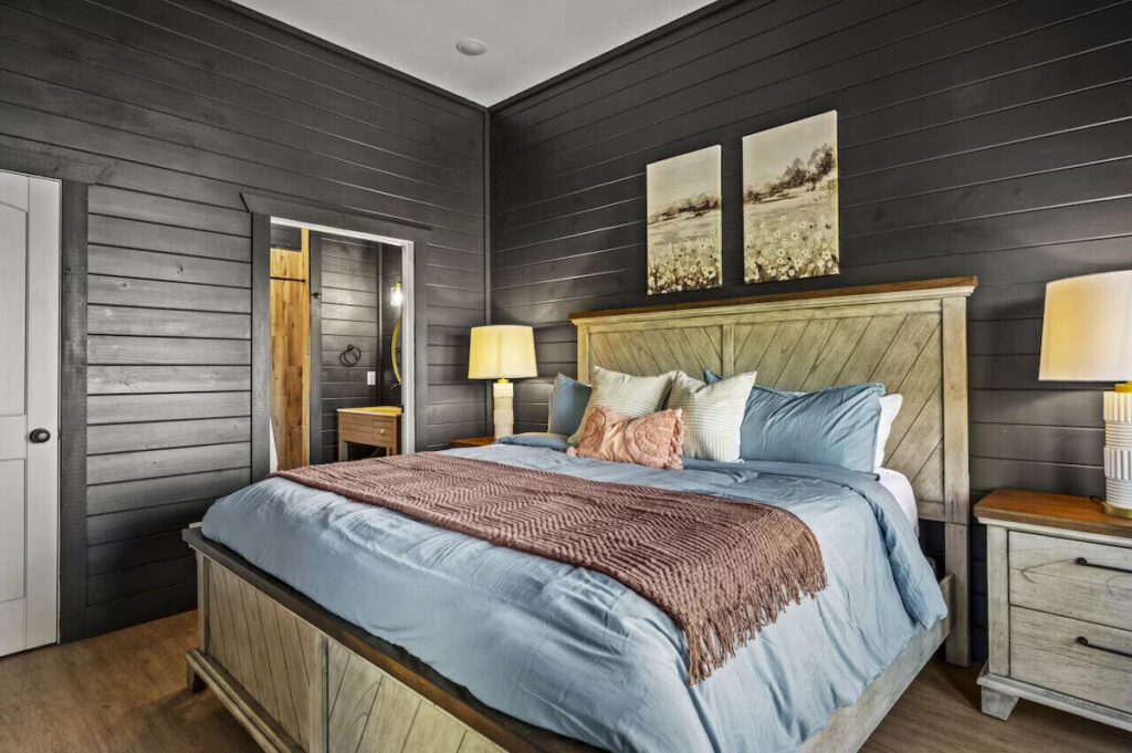 MCHB luxury primary master suite in Sevierville, TN. Features bold blacked-out walls, a massive bed with custom linens, high-end furniture, and a seamless sliding door transition to the integrated luxury bathroom in a custom cabin.