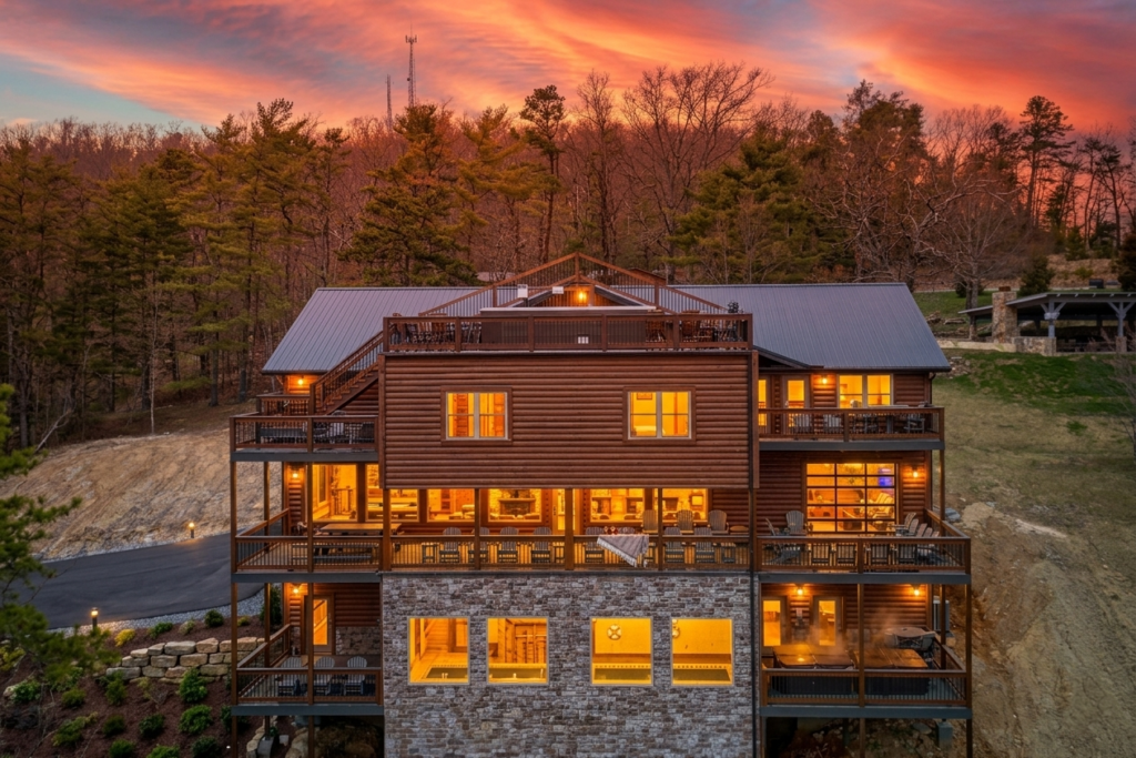 Rear exterior view of a three-story MCHB luxury mountain home in Gatlinburg, TN, featuring an indoor pool, multi-level decks, and a rooftop viewing area.