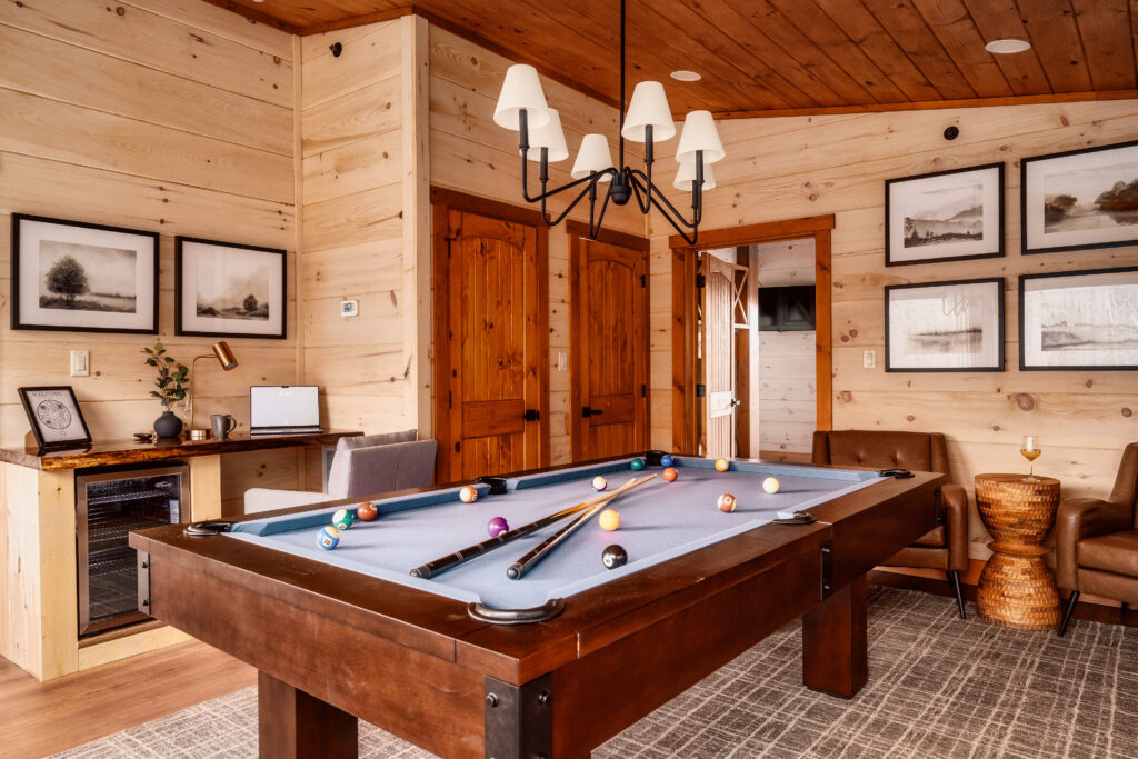 Spacious luxury game room in a Pigeon Forge cabin by MCHB. Features elegant wood finishes, a central pool table, and a balanced distribution of furniture and entertainment elements,