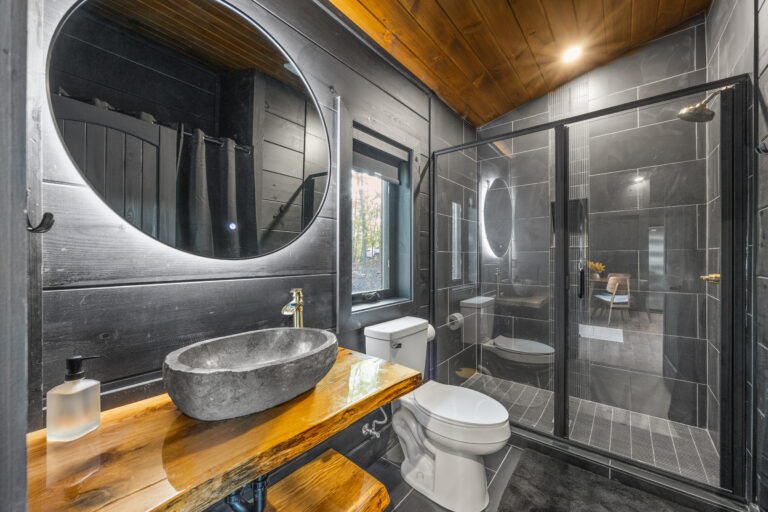 Modern mini cabin bathroom in Gatlinburg featuring a stone sink, lit mirror, elegant tile shower, and wooden table.