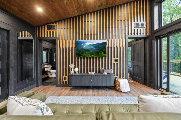 Perspective shot from the living room couch of an MCHB mini cabin, showing wood-detailed walls and partially open doors to the bedroom and bathroom.