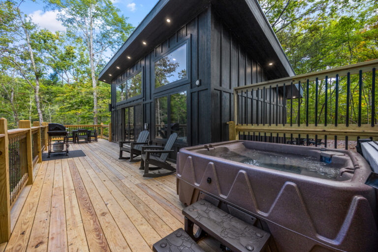 Side perspective of a wooden balcony deck on a mini cabin in Pigeon Forge, featuring a hot tub, BBQ grill, and reclining chairs.