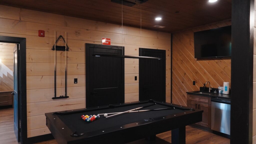 Lower-level luxury game room at 3264 Laurel Cove Trail by MCHB, featuring a custom bar, multicade arcade machine, and a central pool table.