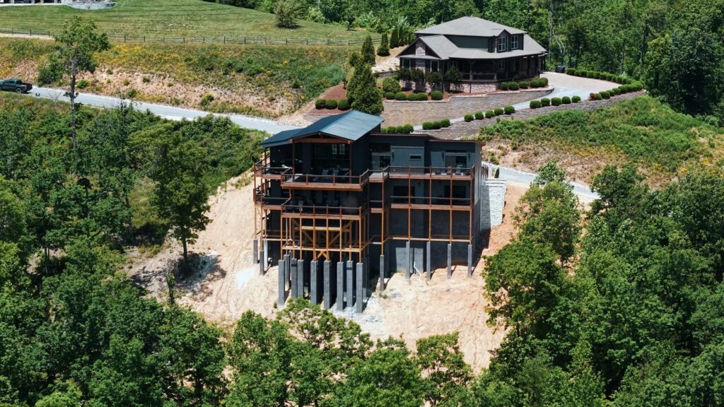 Rear aerial drone shot of 3264 Laurel Cove Trail, showing the home's full levels and neighborhood placement nestled among lush trees and opposing mountain homes.