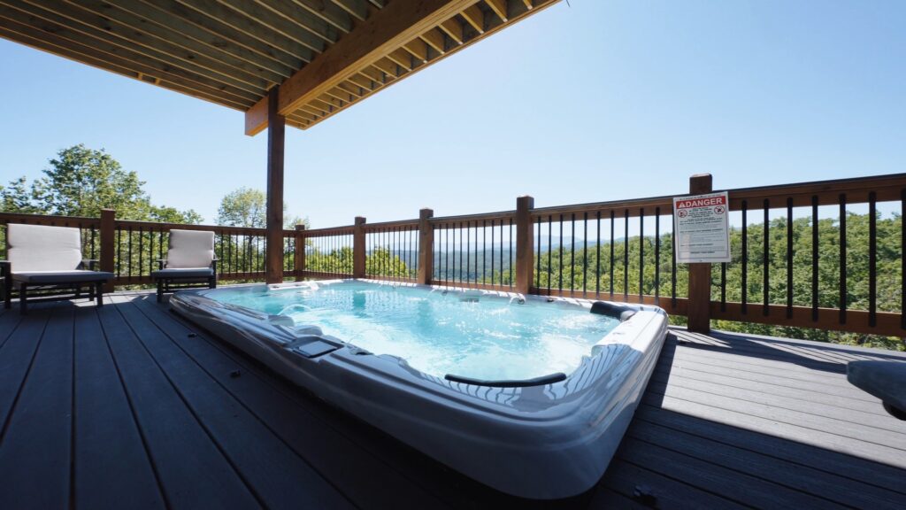 Side view of a luxury cabin deck spa featuring a large hot tub whirlpool, reclining deck chairs, and an open view of the Smoky Mountain skyline.