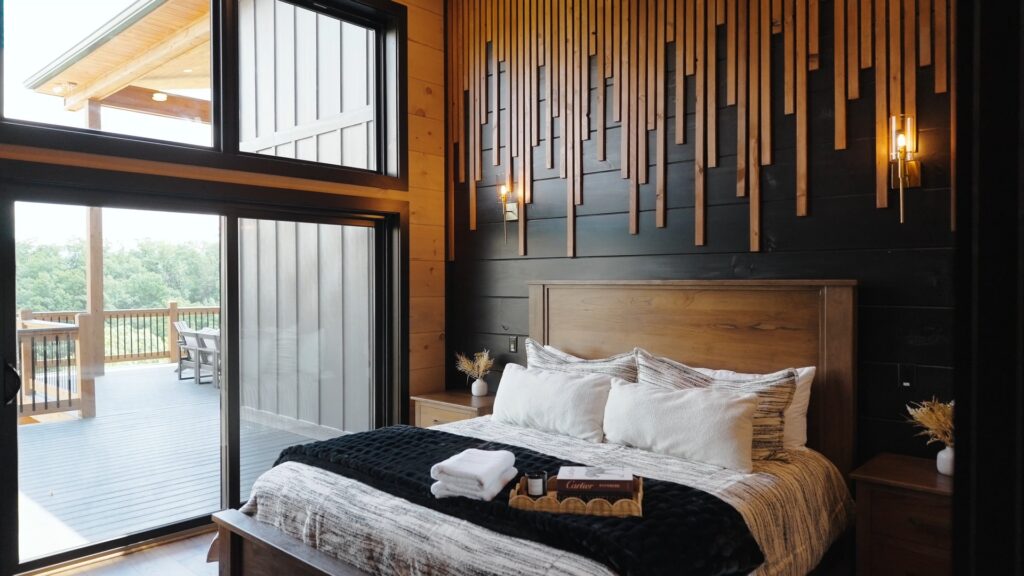 Side shot of a fully furnished main bedroom featuring a custom accent wall, king-size bed, luxurious linens, and a window viewing the terrace deck.