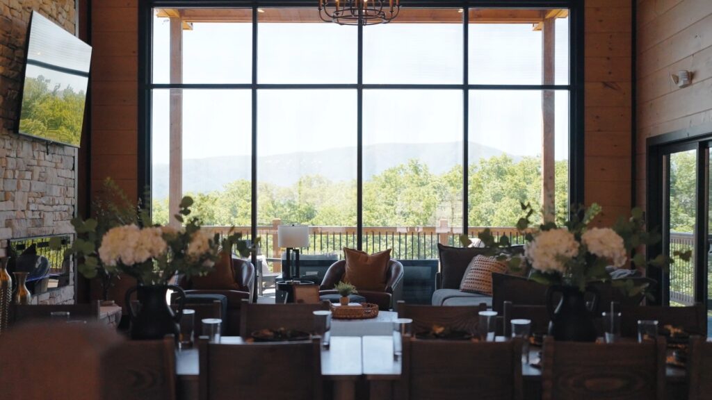 Interior depth-of-field shot with a blurred decorated dining table in the foreground and a focused luxury living room framing a large glass window wall with mountain views.
