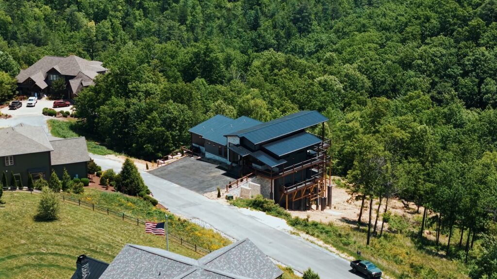 Side aerial drone shot of 3264 Laurel Cove Trail by MCHB in Sevierville, TN, a multi-level luxury cabin surrounded by dense green forest on a spacious residential mountain lot.