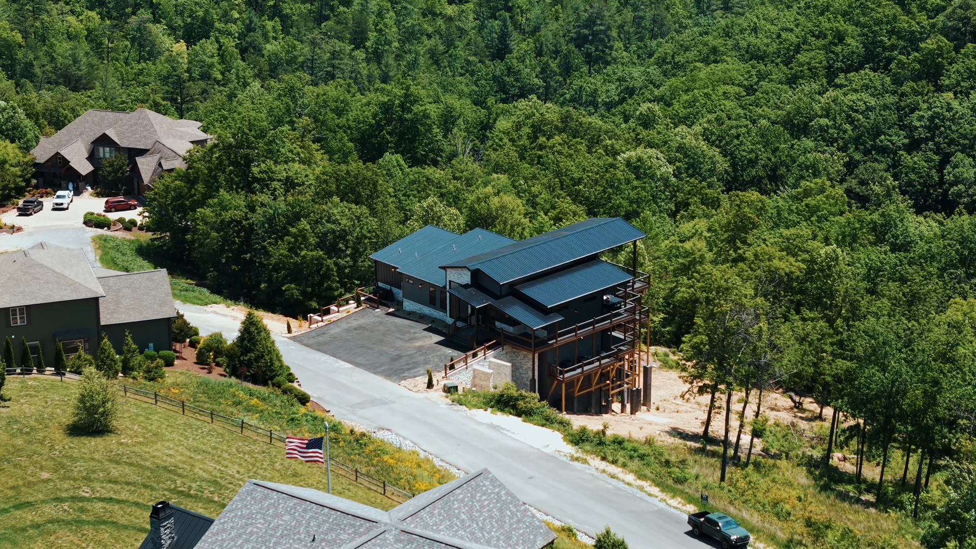Side aerial drone shot of 3264 Laurel Cove Trail by MCHB in Sevierville, TN, a multi-level luxury cabin surrounded by dense green forest on a spacious residential mountain lot.