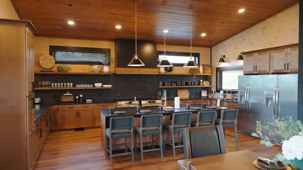 Side shot of a fully custom kitchen at 3264 Laurel Cove featuring two stoves, two large fridges, pop-up shelves, and a marble waterfall island countertop with 5 tall stools.