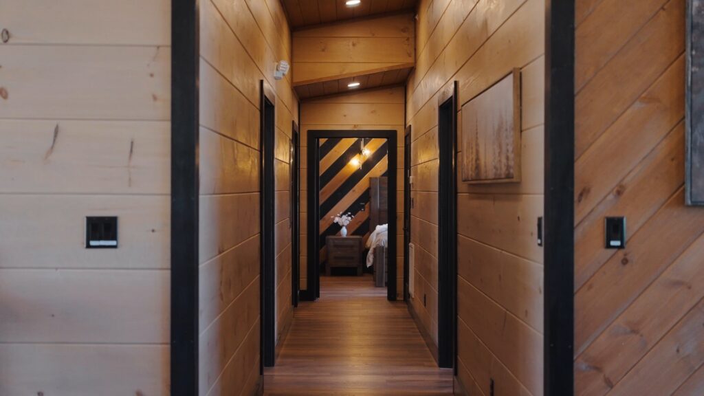 Deep perspective architectural shot of an elegant wood-paneled hallway leading down to a beautifully lit bedroom at 3264 Laurel Cove Trail.