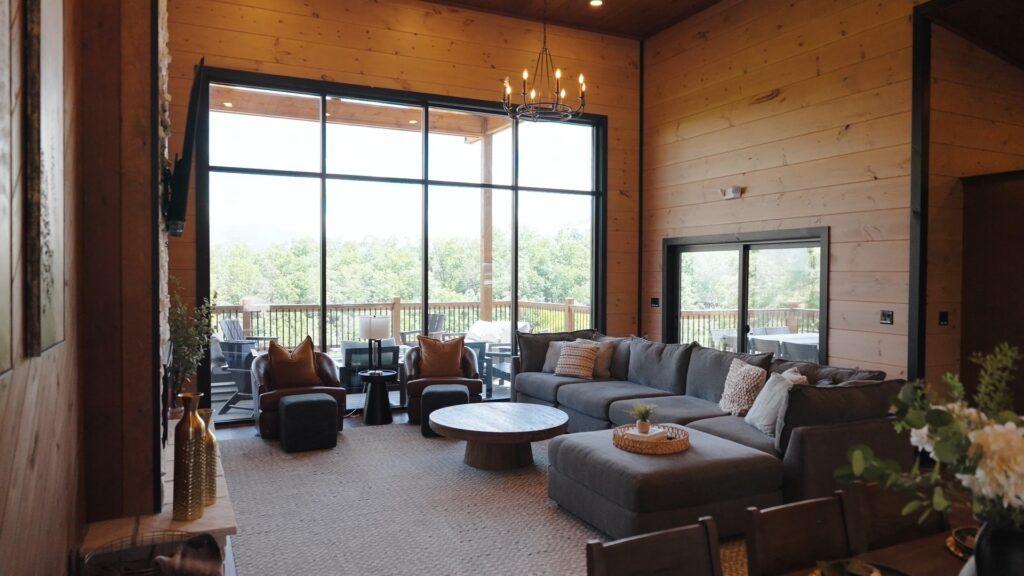 Side shot of the wide living room at 3264 Laurel Cove Trail, showcasing soaring vaulted ceilings, a massive glass window wall, custom furniture, and an access door to the terrace deck.