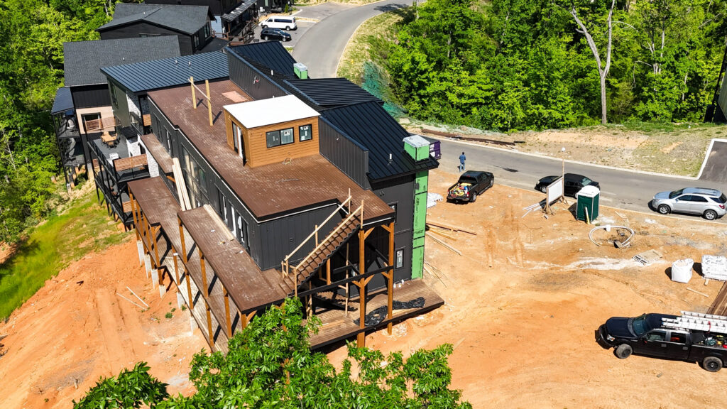 Close-range side aerial drone shot of a multi-level MCHB luxury mountain cabin nearing completion, showing active work staging areas and completed exterior siding.