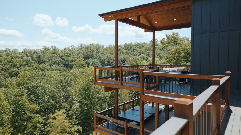 Handcrafted wooden balcony deck of an MCHB luxury cabin in Gatlinburg, TN, featuring premium resort-style outdoor lounging furniture and custom timber structural railings framing a panoramic view of the Smoky Mountains.
