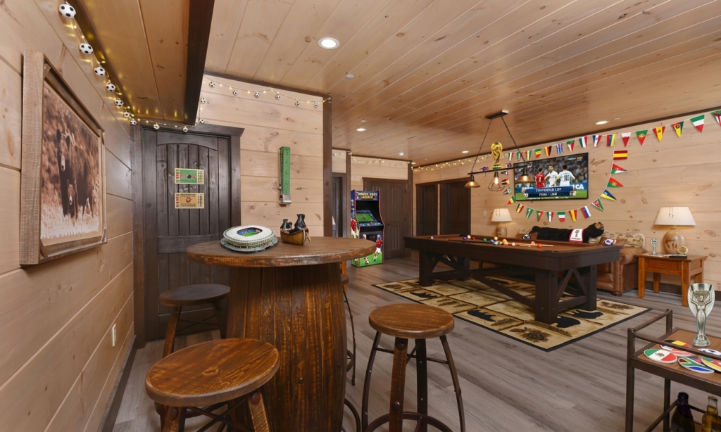 Custom indoor sports bar inside an MCHB luxury cabin, featuring high-top whiskey keg tables, soccer world cup decorations, a pool table, and wall-mounted flat-screen TVs.