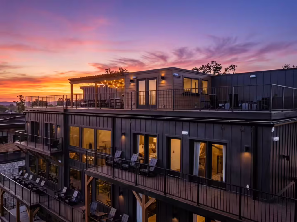 Rear aerial drone view of the completed 7,000 square foot Reedmont Celeste Estate by MCHB at twilight, highlighting stacked multi-level decks and an expansive rooftop event terrace against a sunset backdrop.