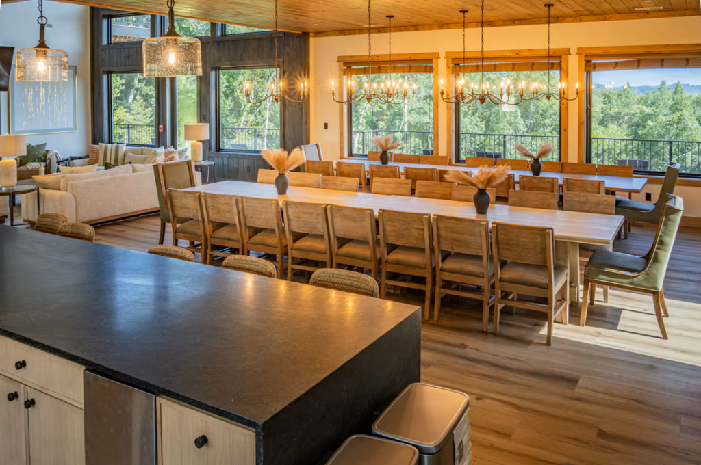 Architectural perspective shot from behind a luxury quartz kitchen island looking through a grand dining area into a sun-drenched mountain living lounge.
