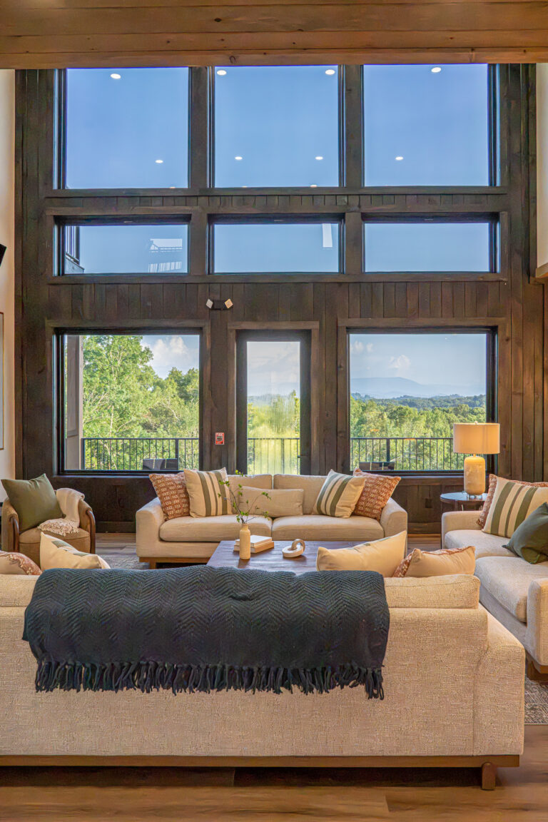 Side interior view of a luxury living room featuring floor-to-ceiling glass wall windows and sliding doors opening toward natural outdoor mountain scenery.