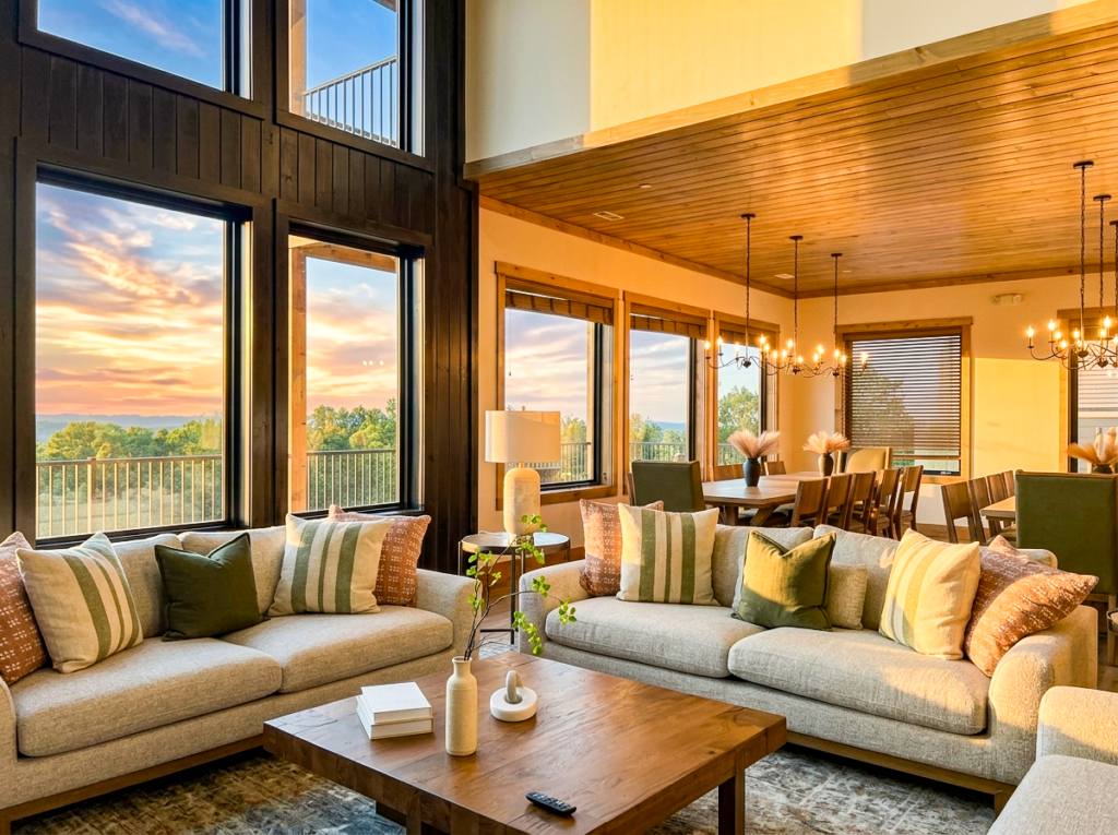 Modern luxury cabin living room filled with golden hour afternoon sunlight, showcasing high-end furnishings, open layout, and summer tree foliage outside