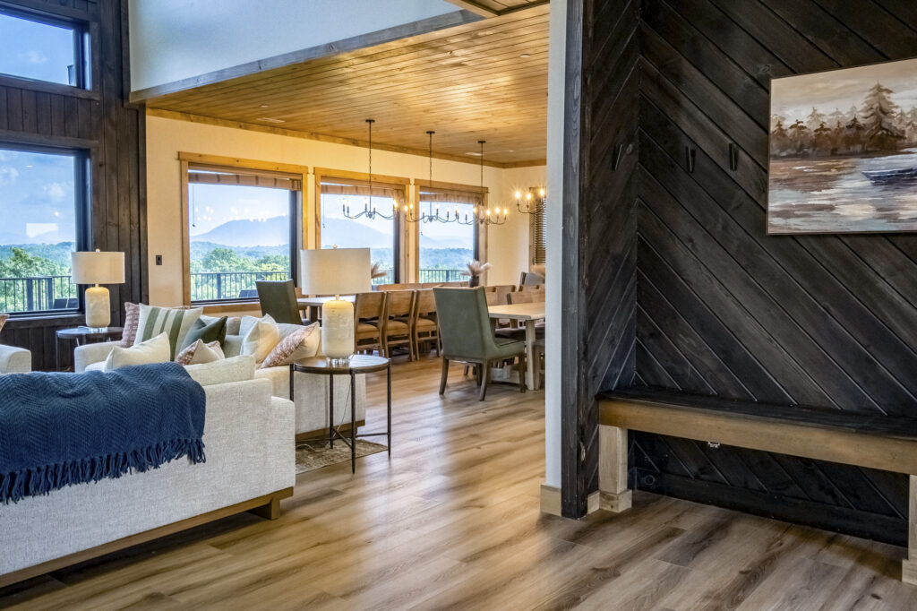 Revealing view from an entryway foyer showing parquet wood floors, textured accent walls, natural light from large windows, and an open dining area in a luxury mountain home.