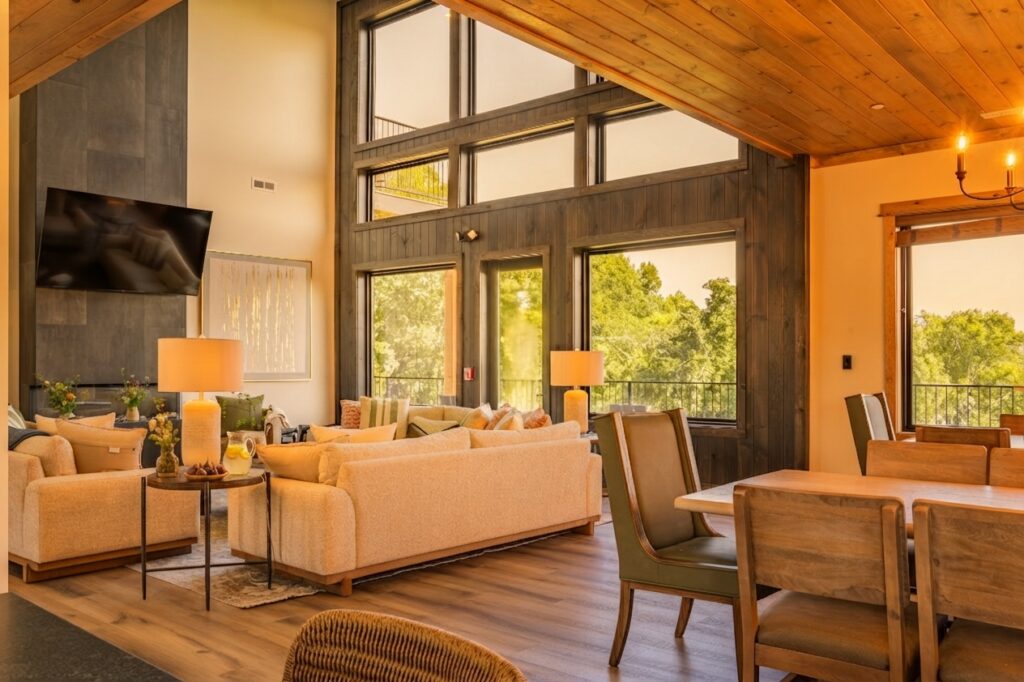 Wide shot of a luxury living and dining room with curated interior decor, floor-to-ceiling glass walls leading to a terrace, and golden hour Smoky Mountain views.