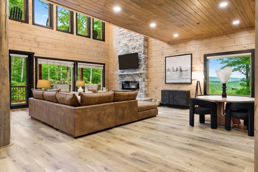 Ample vaulted ceiling in a modern luxury mountain home living room with large glass windows showing lush green summer forest trees built by Mountain Cabin Home Builders.