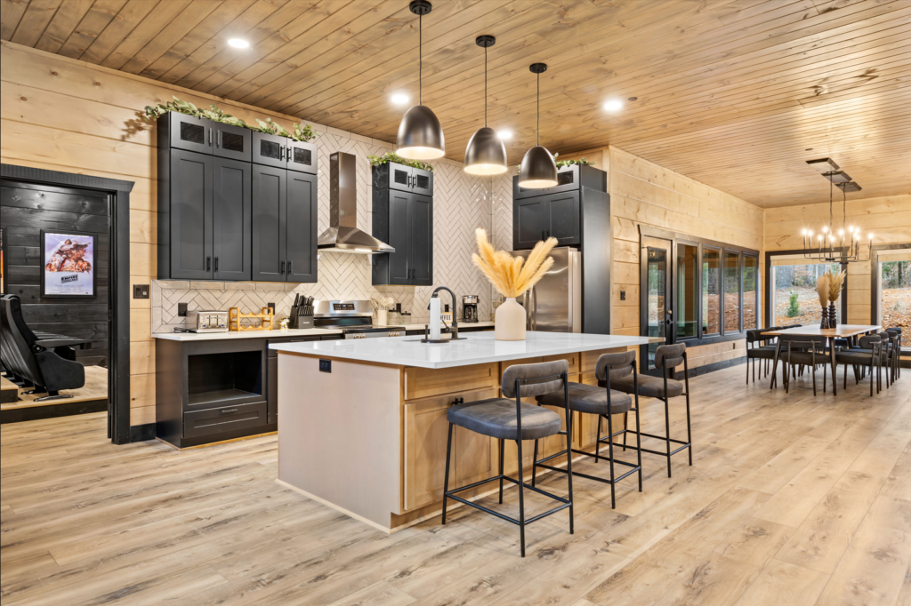 Angled side shot of a modern cabin kitchen featuring a large marble waterfall island, modern bar seating, and linear LED pendant lighting in Gatlinburg